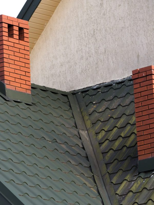 Close-up detail of new modern house top with shingled green roof, high brick-red chimneys and stucco walls. Professionally done building and construction work, real estate property, contract concept.